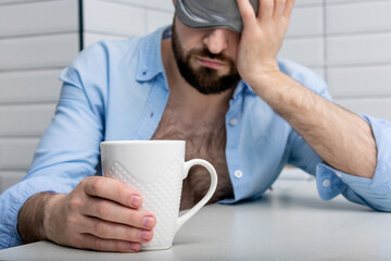 Sleepy man with a cup of coffee in the morning, man in a sleep mask can't wake up, close-up, cropped image