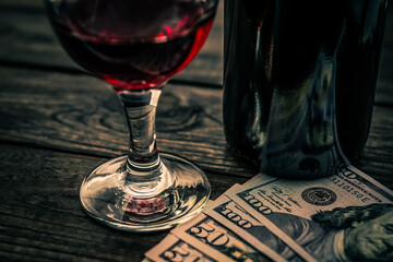 Bottle of red wine with a glass of red wine and money on an old wooden table. Close up view, focus on the glass of red wine