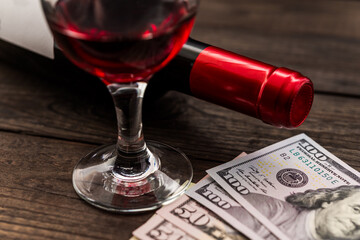 Bottle of red wine with a glass of red wine and money on an old wooden table. Close up view, focus on the glass of red wine