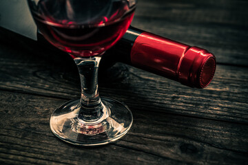 Bottle of red wine with a glass of red wine on an old wooden table. Close up view, focus on the glass of red wine