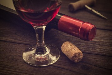 Bottle of red wine with a glass of red wine and cork on an old wooden table. Close up view, focus on the glass of red wine