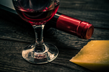 Bottle of red wine with a glass of red wine and a pice of parmesan on an old wooden table. Close up view
