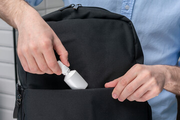 Man puts nose drops, spray in a backpack, male hands, cropped image, close-up
