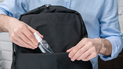 Man puts sanitizer or antiseptic,  in a backpack, male hands, cropped image, close-up