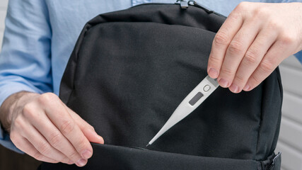 Person puts electronic thermometer in a backpack, male hands, cropped image, close-up