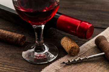 Bottle of red wine with a glass of red wine and cuban cigar with corkscrew on an old wooden table....