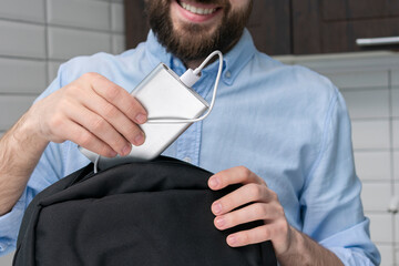 Man puts power bank in a backpack, male hands, cropped image, close-up