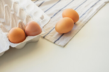 Chicken brown eggs in an egg container, white table, cropped image