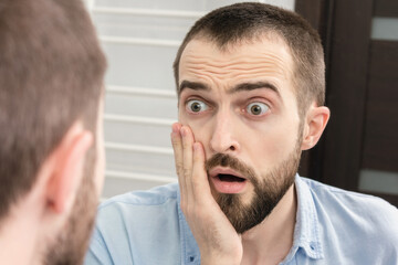 Fototapeta premium Shocked man seeing something surprising in bathroom mirror, portrait, closeup