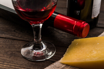 Two bottles of red wine with a glass of red wine and a piece of parmesan on an old wooden table. Close up view, focus on the bottle of red wine