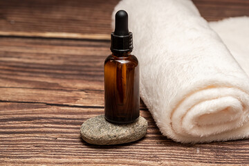 Cosmetic oil stands on a stone. There is a white towel next to it.