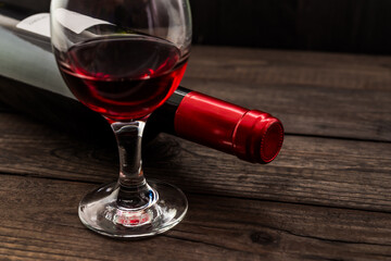 Bottle of red wine with a glass of red wine on an old wooden table. Angle view, focus on the glass of red wine