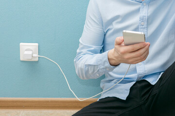 Phone when it is charging, man with phone and battery charger with a cable, close-up, cropped image