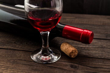 Bottle of red wine with a glass of red wine and cork on an old wooden table. Angle view, focus on the glass of red wine