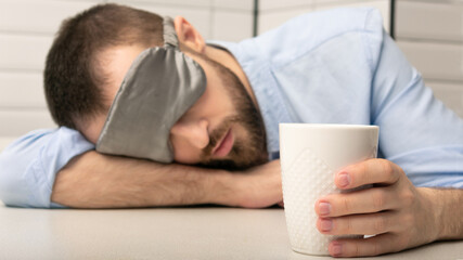 Asleep bearded with a cup of coffee in the morning, man in a sleep mask can't wake up, close-up, cropped image, 16:9