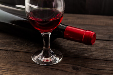 Bottle of red wine with a glass of red wine on an old wooden table. Angle view, focus on the glass of red wine