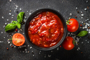 Tomato sauce in a bowl with spices, herbs and fresh tomatoes. Top view at black background.