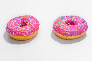 Two pink donut with bright sprinkles, white background, side view, copy space