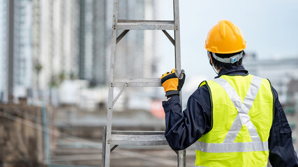 Asian maintenance worker man with safety helmet and reflective suit carrying aluminium step ladder at construction site. Civil engineering, Architecture builder and building service concepts