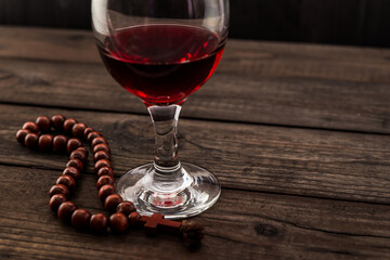 Glass of red wine and rosary on an old wooden table. Angle view, focus on the glass of red wine