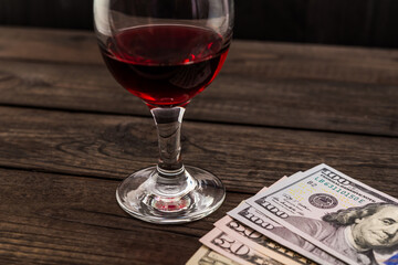 Glass of red wine and money on an old wooden table. Angle view, focus on the glass of red wine