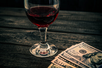 Glass of red wine and money on an old wooden table. Angle view, focus on the glass of red wine