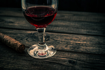 Glass of red wine and cuban cigar on an old wooden table. Angle view