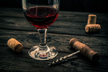 Glass of red wine and corkscrew with corks on an old wooden table. Angle view
