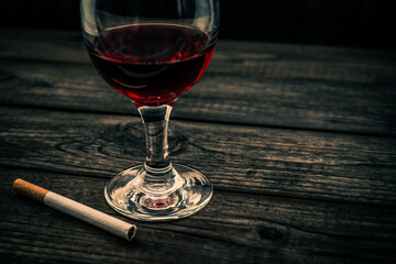 Glass of red wine and cigarette on an old wooden table. Angle view, focus on the glass of red wine
