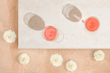 Summer afternoon leisure scene with wine glasses on white marble and white rose flowers in full bloom on orange beige background. Sun and shadows. Minimal flat lay. Vacation concept.