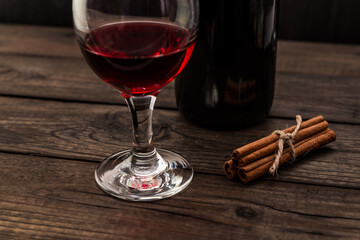 Bottle of red wine with a glass of red wine and  cinnamon sticks tied with jute rope on an old wooden table. Angle view, focus on the glass of red wine