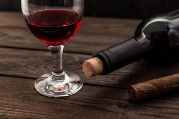 Bottle of red wine with a glass and cuban cigar on an old wooden table. Angle view