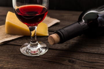 Bottle of red wine with a glass and a piece of parmesan on an old wooden table. Angle view