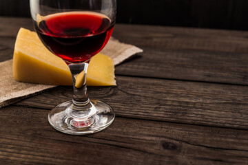 Glass of red wine with a piece of parmesan on an old wooden table. Angle view