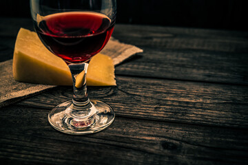 Glass of red wine with a piece of parmesan on an old wooden table. Angle view