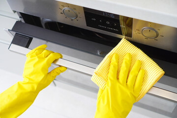 Cleaning service or housework. Female hand in a yellow rubber glove wipes built-in oven in a...