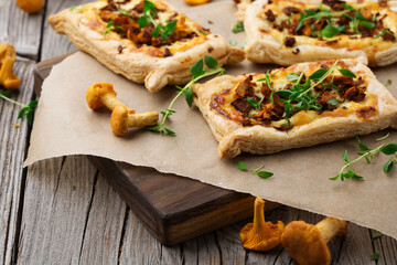 Homemade tarts of puff pastry with seasonal chanterelle mushrooms on rustic table. - obrazy, fototapety, plakaty