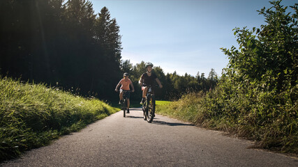 Naklejka premium Mother and daughter riding mountain bikes in the country road in green nature on a sunny day.