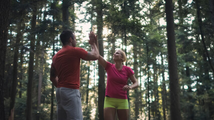 Smiling Caucasian couple running in the forest, at the end of the run giving high five to each other