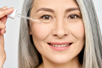 Closeup cut portrait of senior mature older Asian woman touching clean face eye contour with...