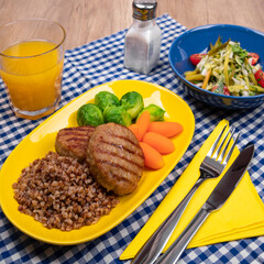 Meat cutlets with buckwheat, baby carrots, green brussel sprouts vegetable and fresh salad. Served on plate on wooden table. Orange juice. Delicious lunch.