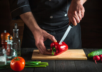 Professional chef or cook cutting red peppers for salad on restaurant kitchen table. Vegetable diet or snack idea