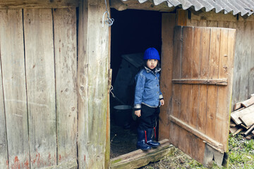 Fototapeta premium country boy stands next to a barn in a doorway in warm clothes