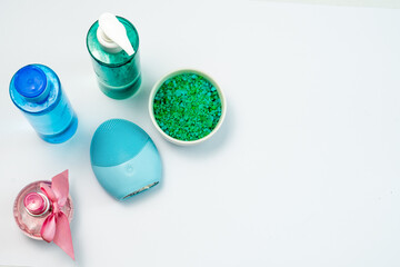Cosmetic flat lay: health care products, bath salt and facial massager in green and blue colours on a white background. Natural organic product, beauty and spa concept
