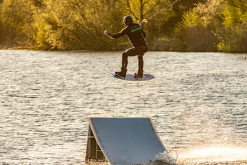 Wakeboarder making tricks. Low angle shot of man wakeboarding on a lake. Man water skiing at sunset.