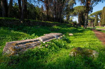 Detail of the marble ruins of Roman tombs on the Appia Antica. The tombs are illuminated by the sun with the blue sky, the pines, the cypresses and the green of the grass. Regina Viarum, Rome Italy.Eu