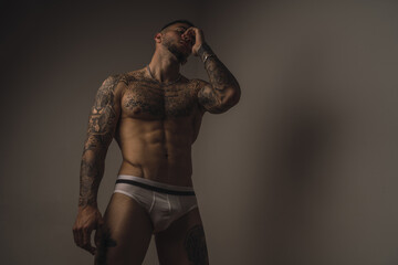 Young handsome muscular Caucasian male with tattoos wearing underwear and posing in a studio