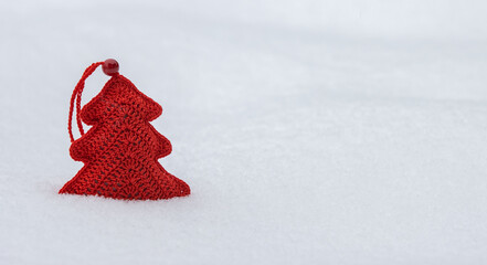 Red knitted toy on white snow.