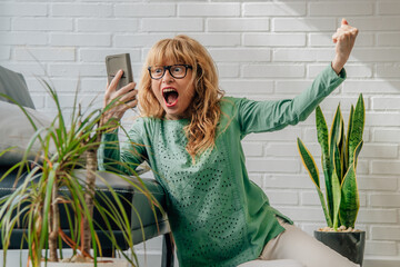 woman with mobile phone at home celebrating enthusiastically