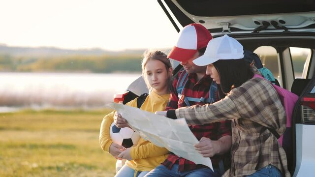 Happy family on a road trip in their car. Dad, mom and daughter open map planning a traveling by the sea or the ocean or the river. Summer road trip by automobile. Travel vacations and family concept.